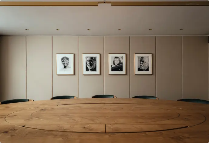 Four framed photos hanging horizontally on a wall. A brown wooden roundtable with five black chairs tucked in.