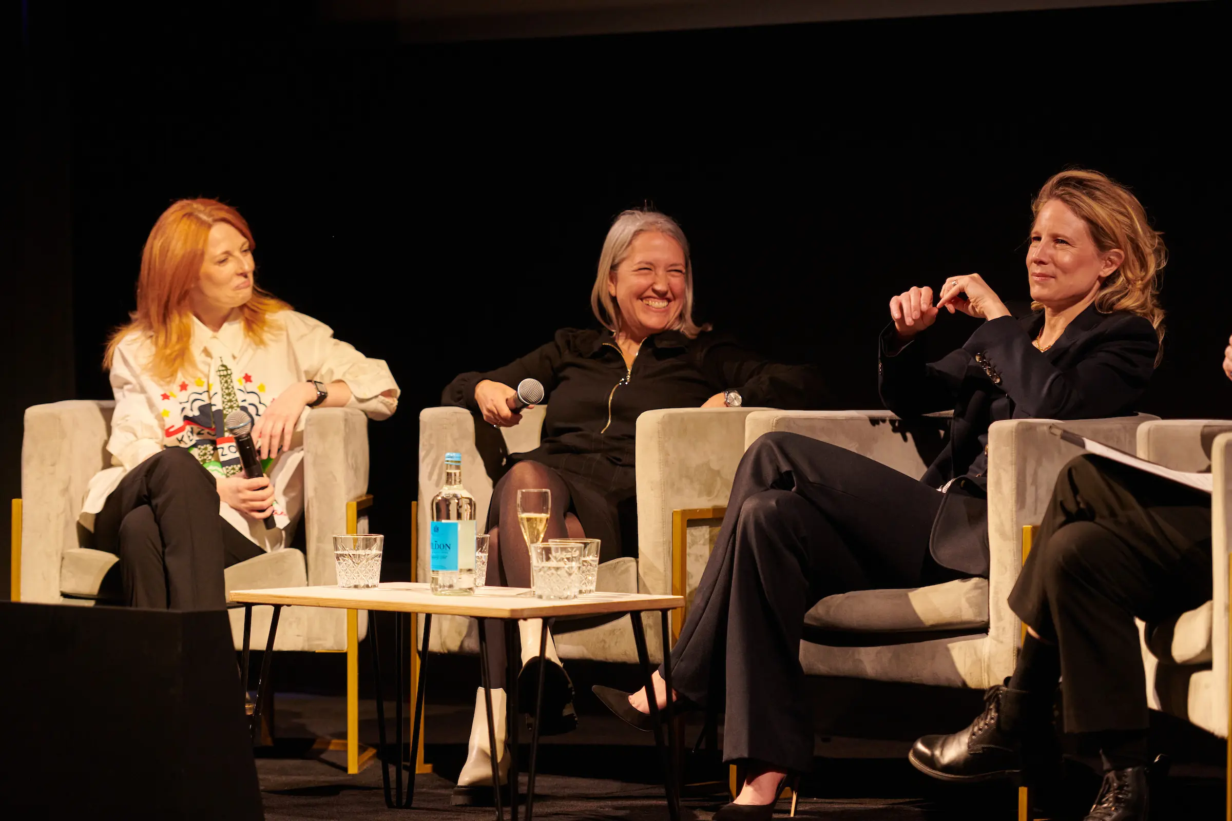 Three women sat on stage having a conversation with microphones.