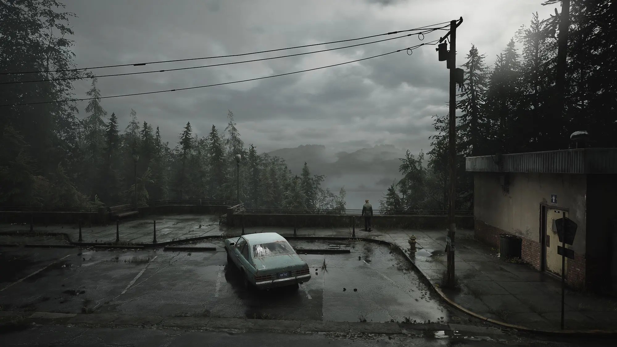 A bleak looking car park overlooking a lake. There is a parked car and a figure in the distance.