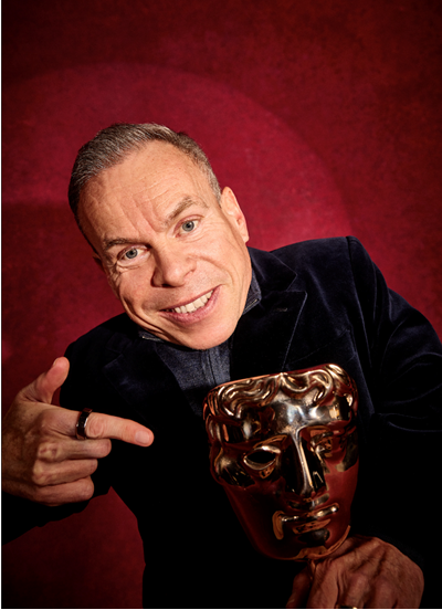 Warwick Davis pointing at his BAFTA Award